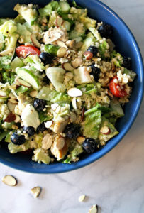 Bowl filled with dairy free salad including romaine lettuce, quinoa, blueberries, chicken, and almonds