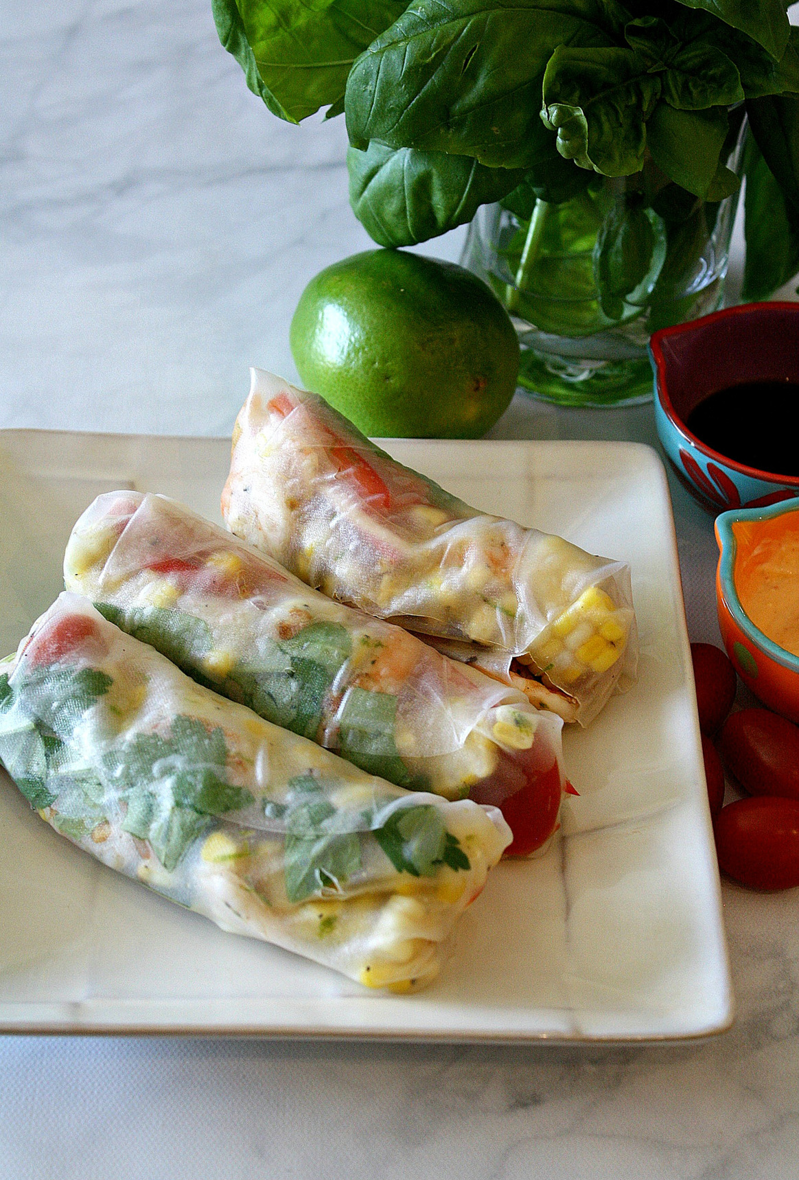 White plate with spring rolls, a lime, basil, and 2 sauces