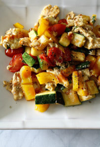 White plate with zucchini, yellow peppers, tomatoes, scrambled eggs, and basil