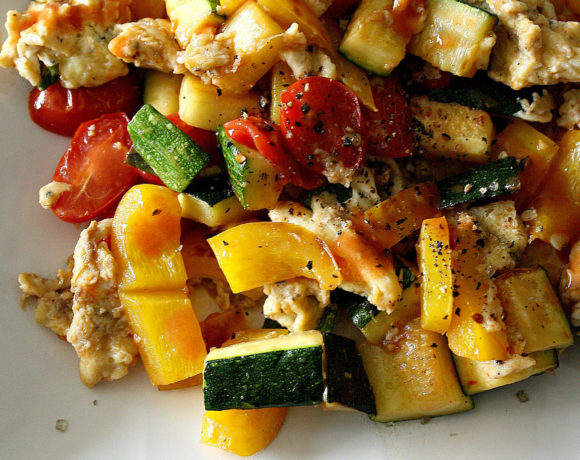 White plate with zucchini, yellow peppers, tomatoes, scrambled eggs, and basil