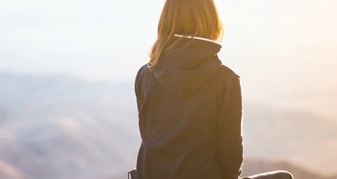Woman sitting on cliff staring into horizon