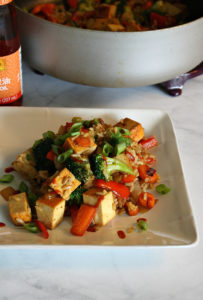 White plate on marble surface with stir fry vegetables and tofu