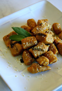 White plate on marble surface with pumpkin gnocchi and sage