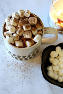 Mug with hot chocolate, marshmallows, and candle on white surface