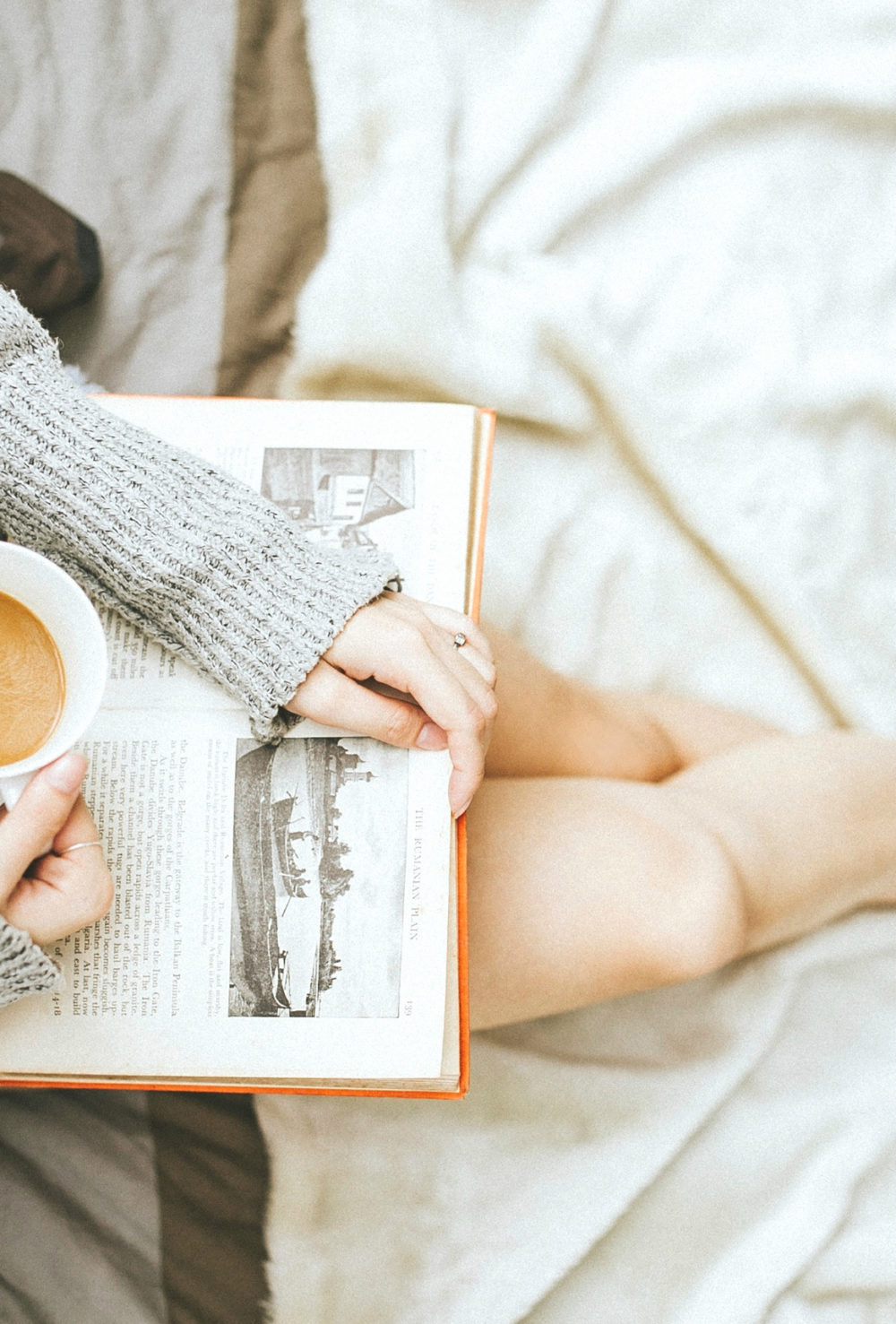 Woman sitting on white blanket reading with coffee